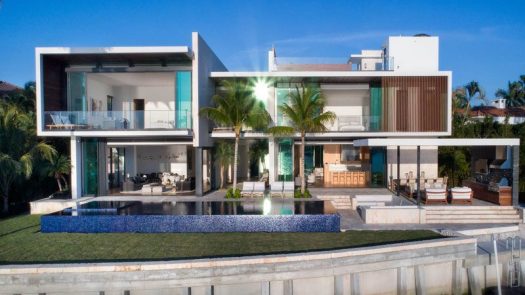 This modern house in Miami has a swimming pool and an outdoor entertaining area with a sunken lounge, outdoor kitchen, as well as an outdoor dining area.