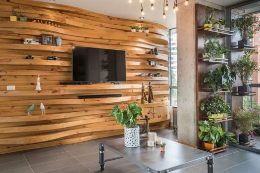 This modern apartment features a wavy wood accent wall that adds warmth to the interior, and also doubles as shelving for the television and decorative home decor items.