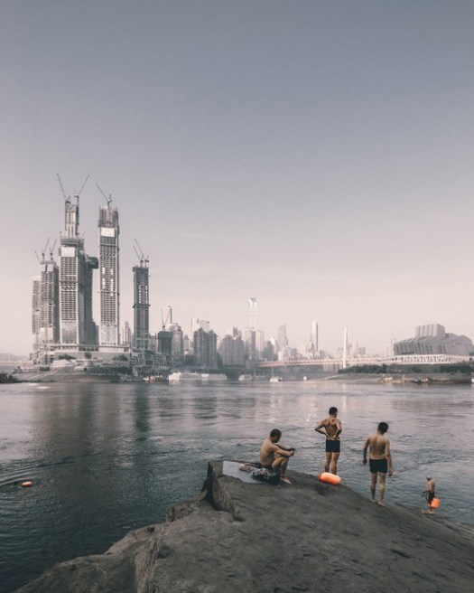 Swimmers on the riverside opposite the construction of Raffles City Chongqing, China by Sadfie Architects. Image © Zhu Wenqiao